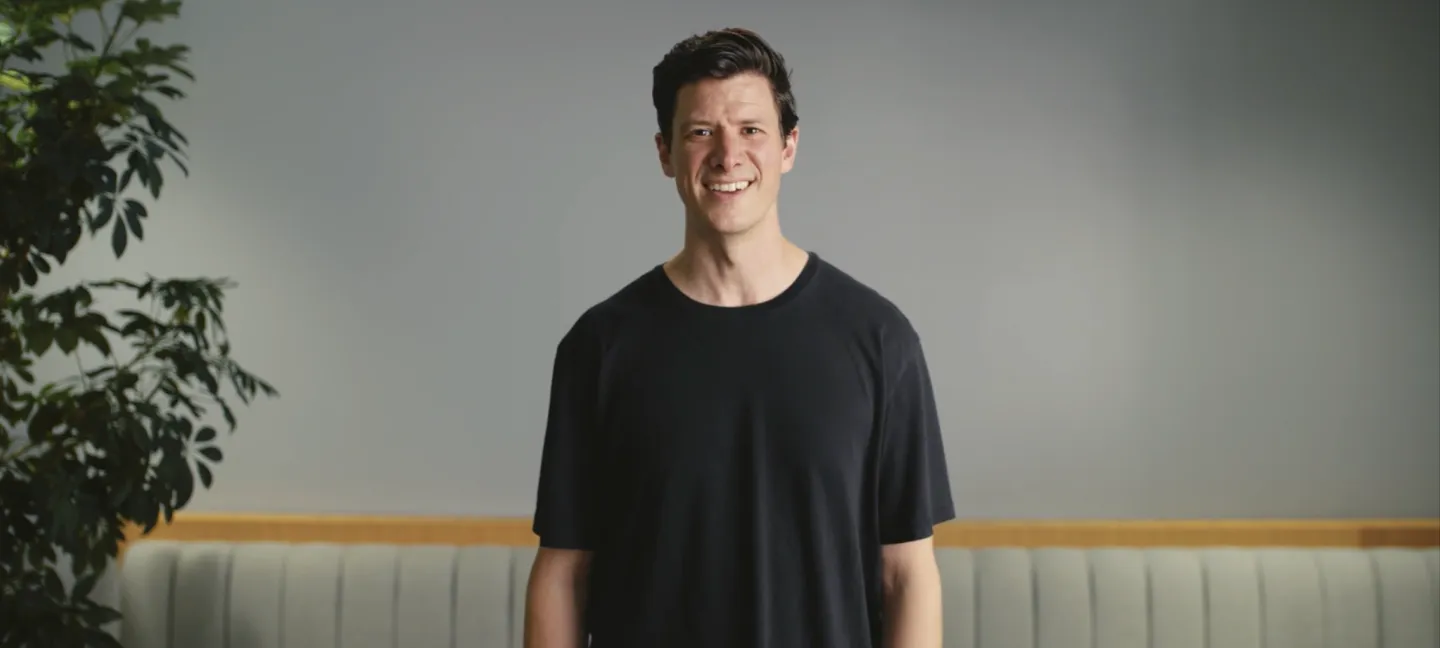 A video of Andrew Farah, creator of Routines, dressed in black t-shirt smiling while standing in a softly lit room and sharing how Routines helps caregivers support loved ones from anywhere.